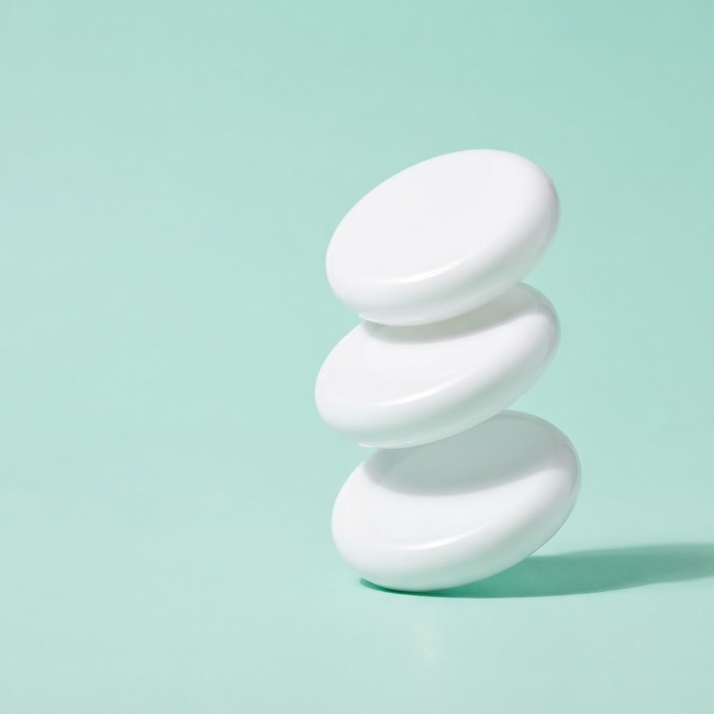 Three glossy white discs stacked at a tilt on a pastel mint background
